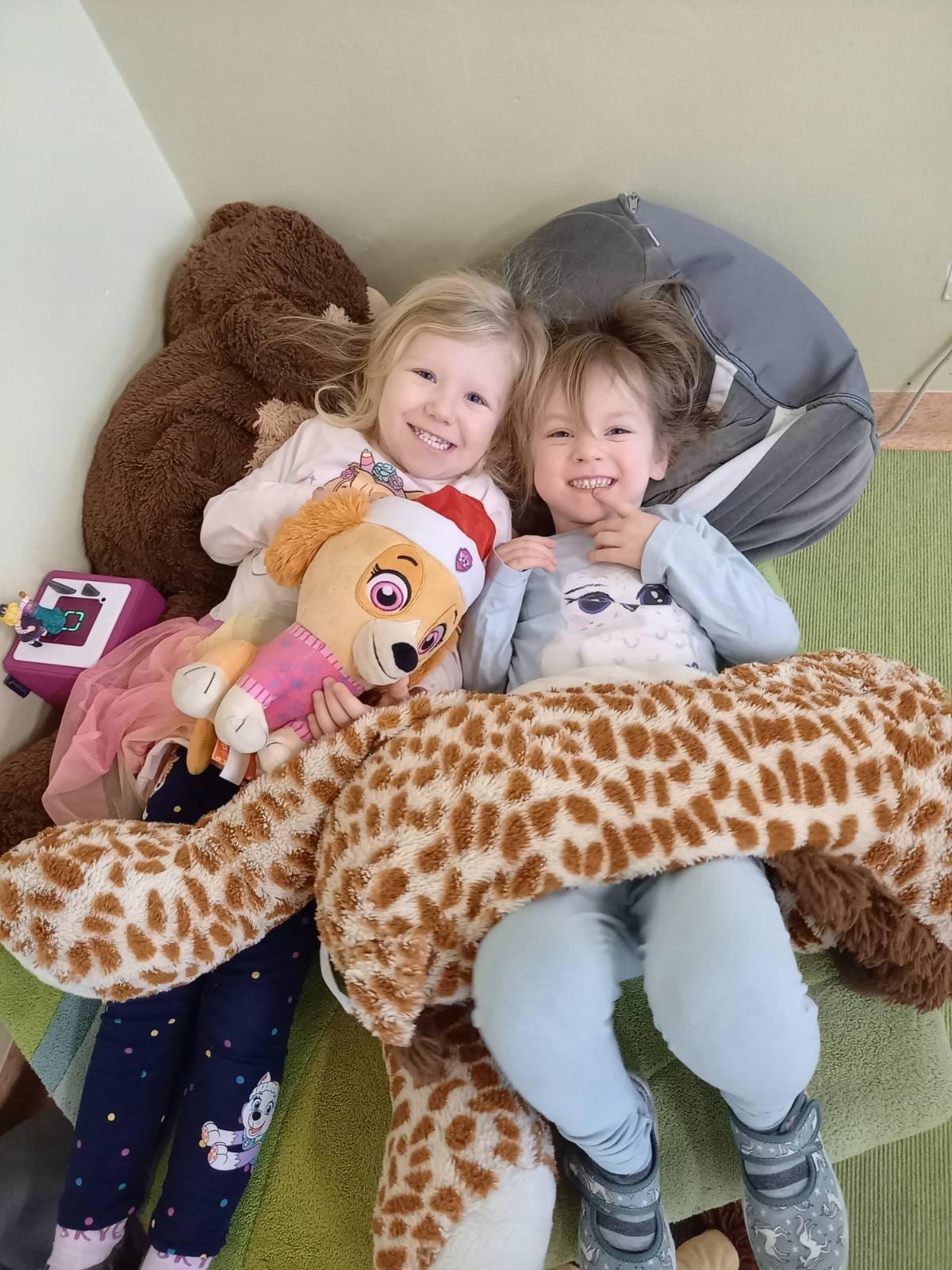 zwei lachende Kinder am Boden mit Kuscheltieren